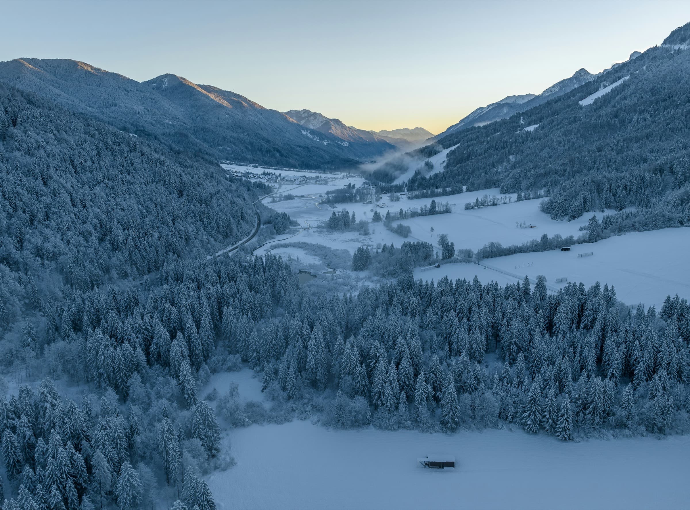 A snowbound alpine valley at dawn, the far ridgeline just catching light